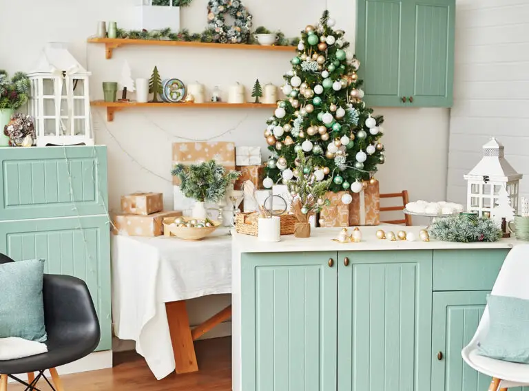 Kitchen and dining area with sage green cabinets, cream walls, wooden shelves, and a decorated Christmas tree.