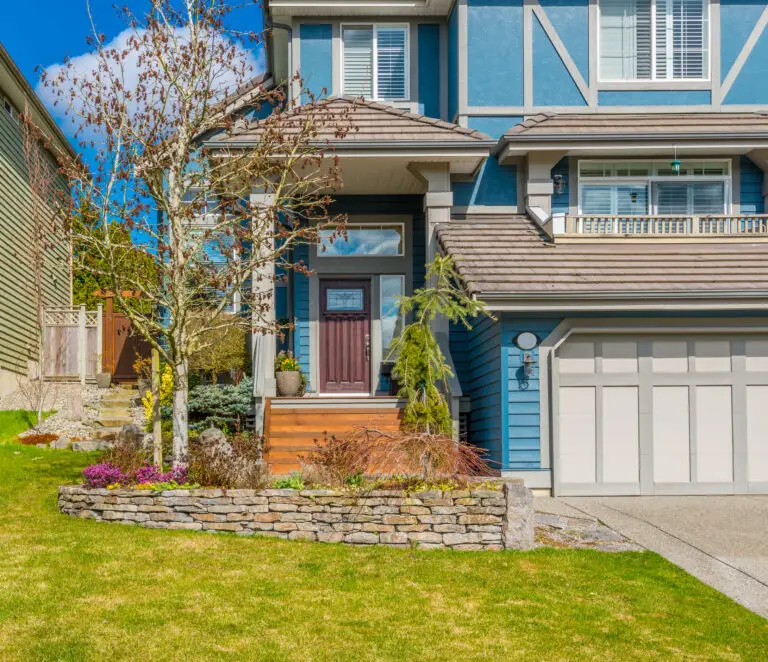Blue two-story house with white trim, a red front door, and a landscaped front yard.